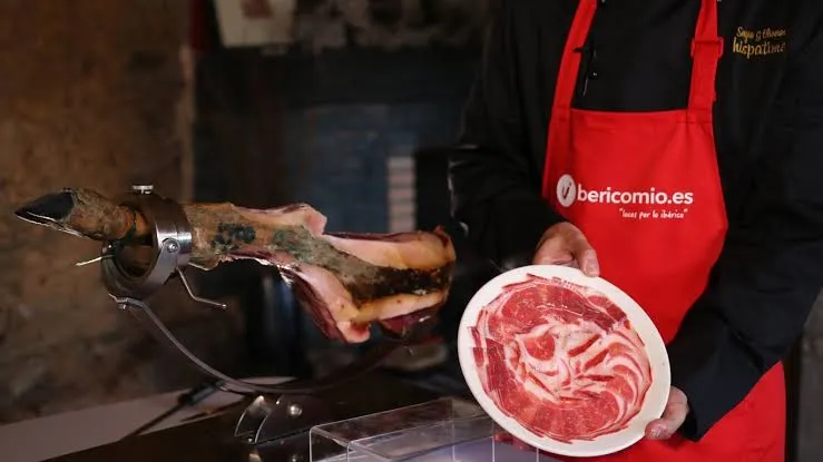 Master ham carver slicing Iberian ham wearing an Ibericomio apron